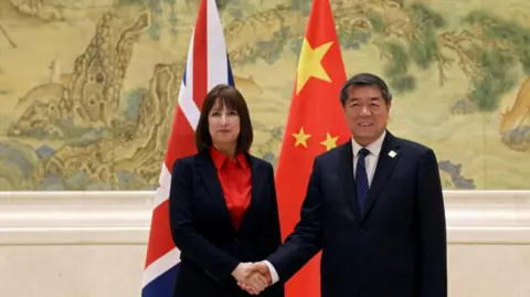 Reuters Chinese Vice-Premier He Lifeng and Britain's Chancellor Rachel Reeves shake hands before flags of China and the UK at a summit in Beijing