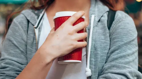 Getty Images Woman wearing grey hoody holding a red disposable coffee cup close to her chest