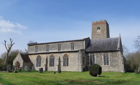 Bats in Churches Exterior of Guestwick Church in Norfolk taken on a clear winter's day. The view is of the side of the church - it's walls are made from grey flint stone, and it has arched stained glass windows and a tower. In the foreground there are some gravestones on a green lawn.